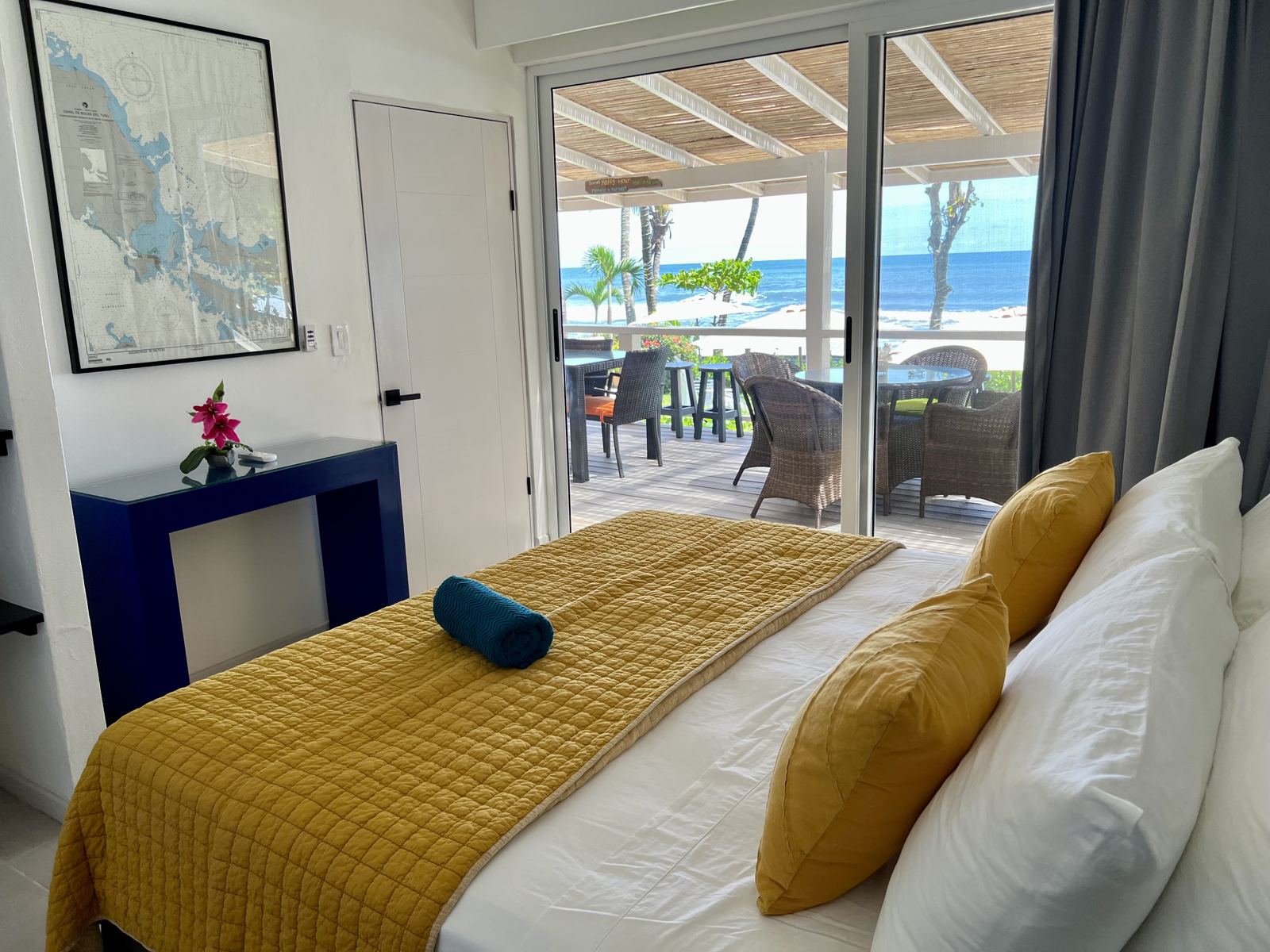 Bedroom with a king bed, yellow throw and glass doors out to the deck and the sea