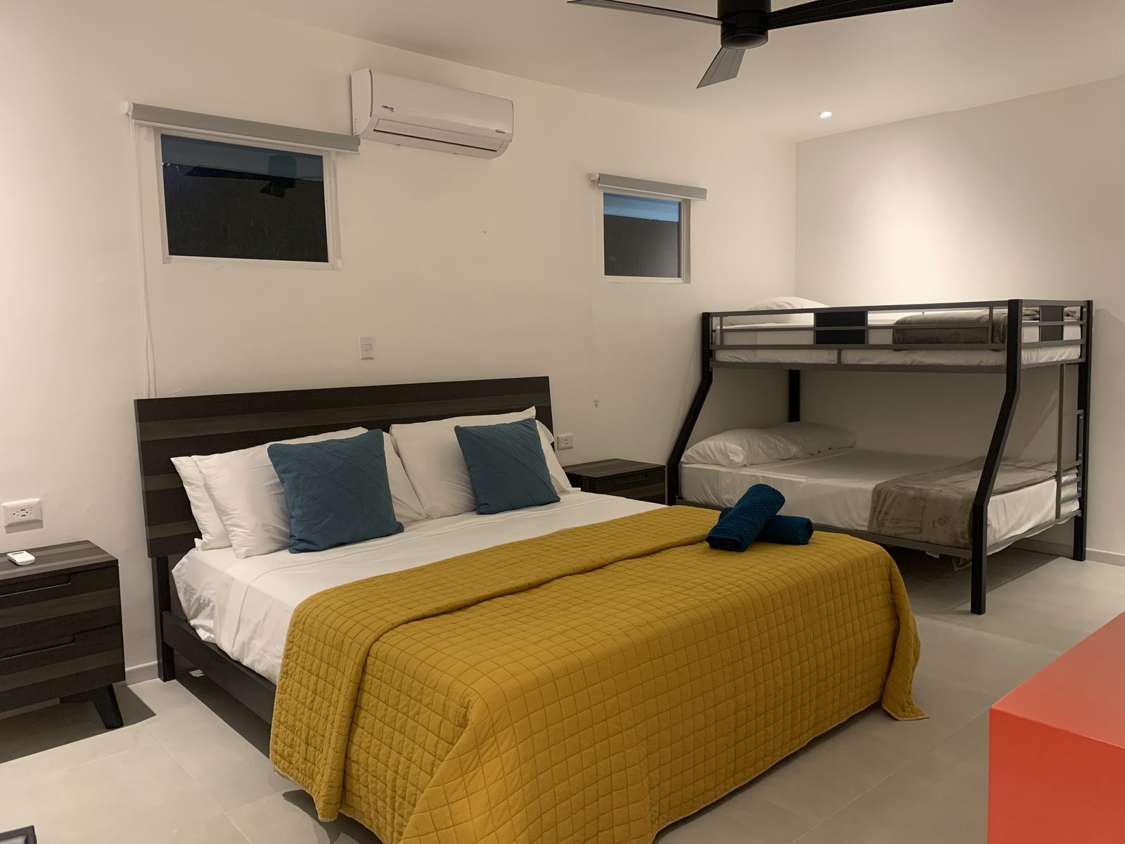Bedroom with a king bed in a mustard quilt and teal pillows beside a full-over-twin bunk bed