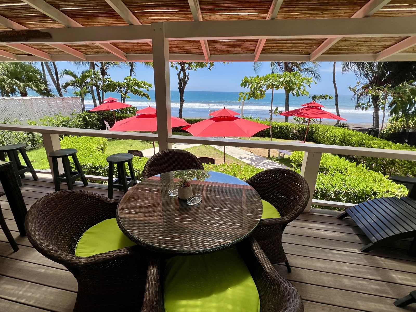 Covered deck with a round table and chairs looking out over the garden to the ocean