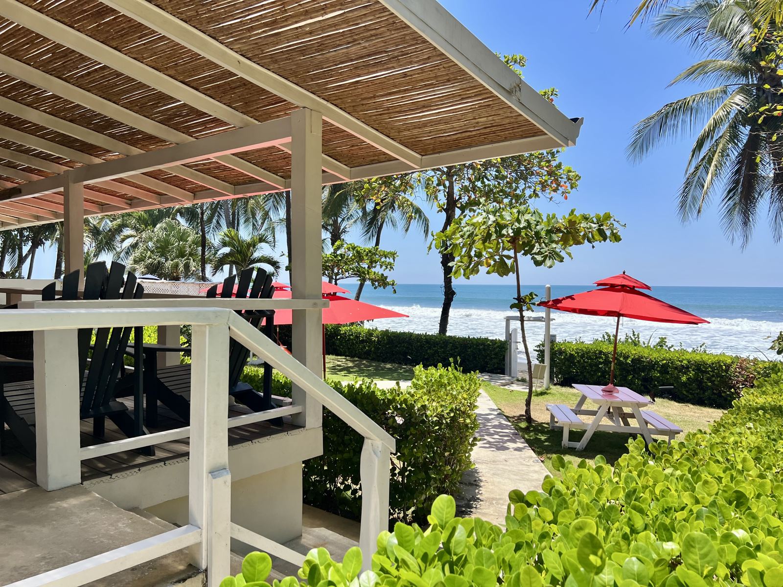 Steps down from the porch through the tropical garden toward the beach and red umbrellas